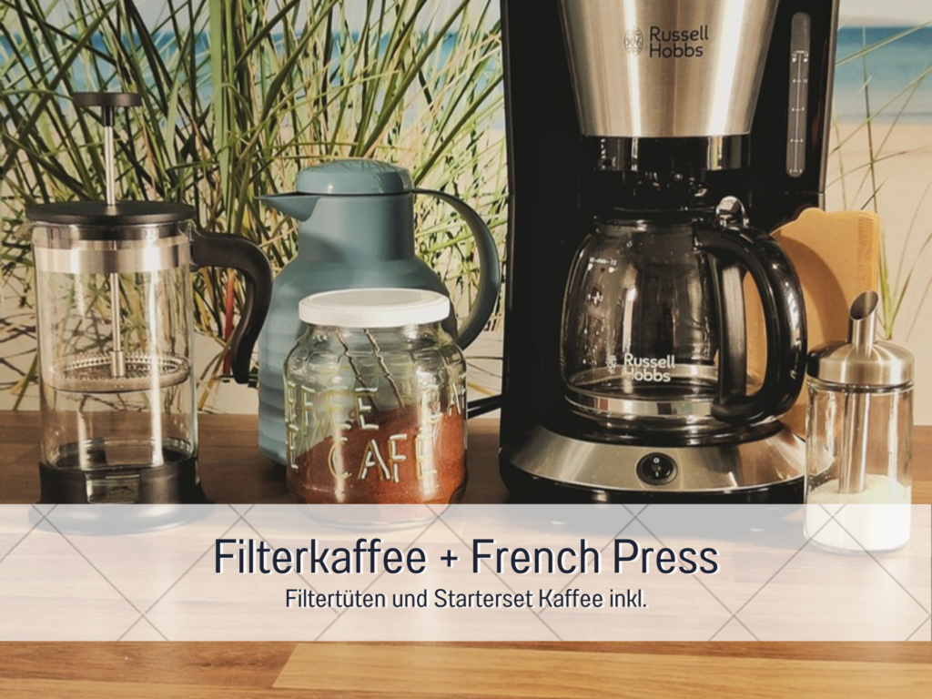 Kaffeemaschine, French Press und Kaffeedose auf einer Küchenarbeitsplatte mit Strandmotiv-Rückwand.