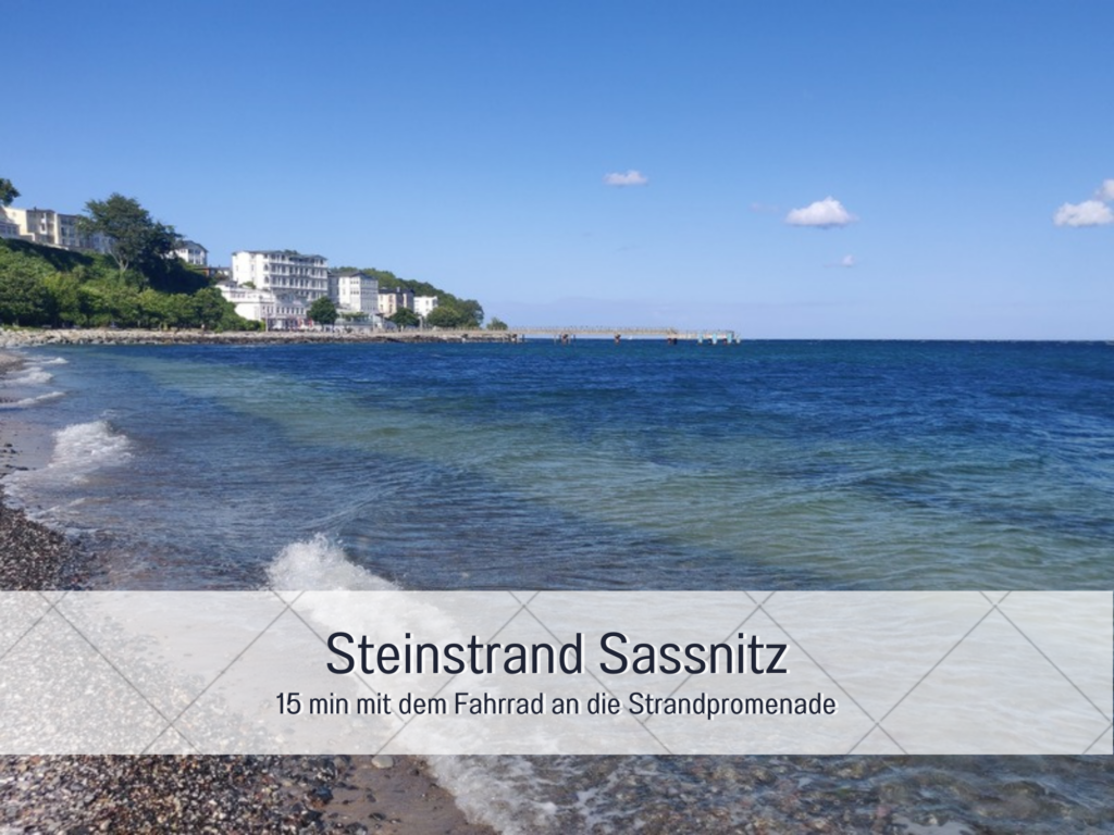 Steinstrand in Sassnitz auf Rügen mit Blick auf die Ostsee, sanfte Wellen am Ufer und historische Bäderarchitektur im Hintergrund. Perfektes Ziel für eine Fahrradtour zur Strandpromenade.
